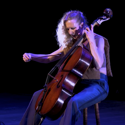 A white woman with blonde hair plays the cello
